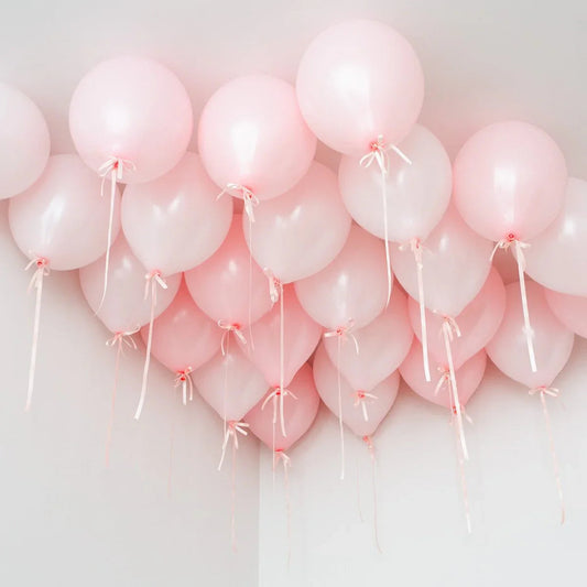 Cluster of pastel pink helium balloons tied with ribbons floating on a white ceiling corner