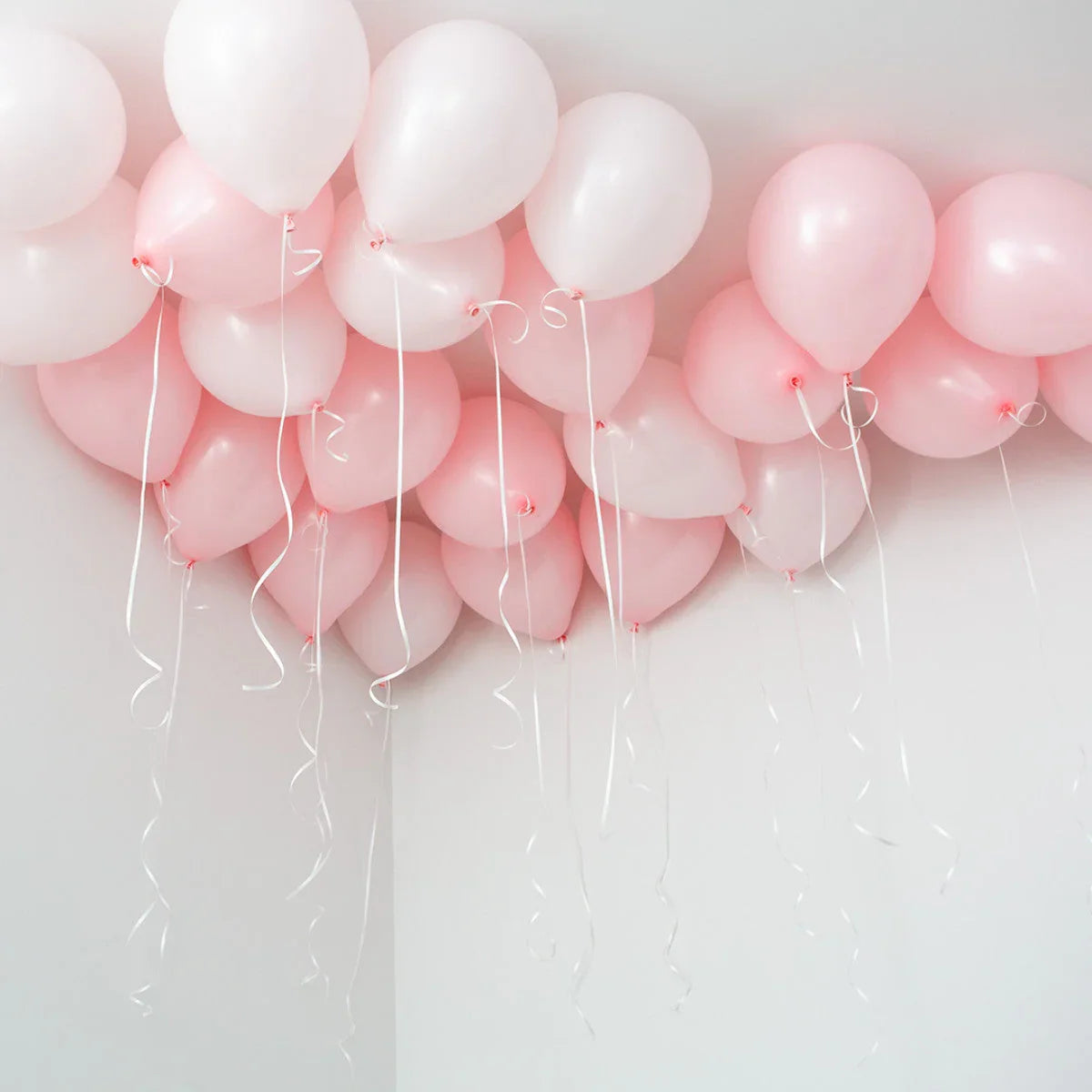 Cluster of pink and white helium balloons floating against a white ceiling with curled ribbons