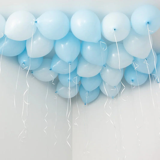Cluster of light blue helium balloons with white curling ribbons floating near a white ceiling
