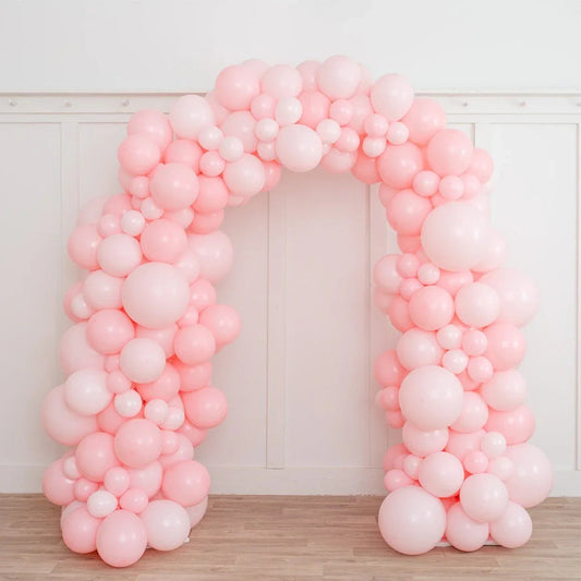 Baby pink balloon arch decoration with various sized balloons in a white room with wooden floor