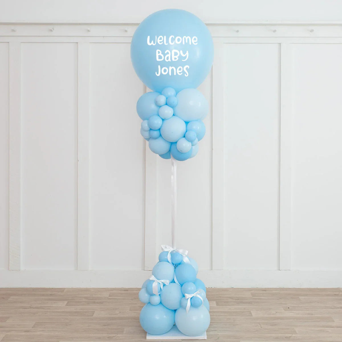 Blue baby shower balloon pillar with welcome baby Jones text in white room