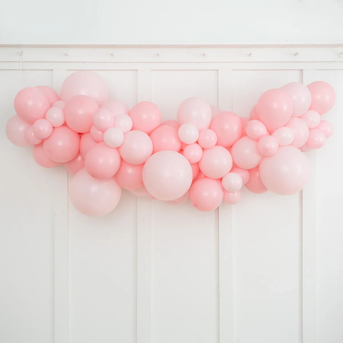 Pink balloon garland decoration with various sizes against white paneled wall