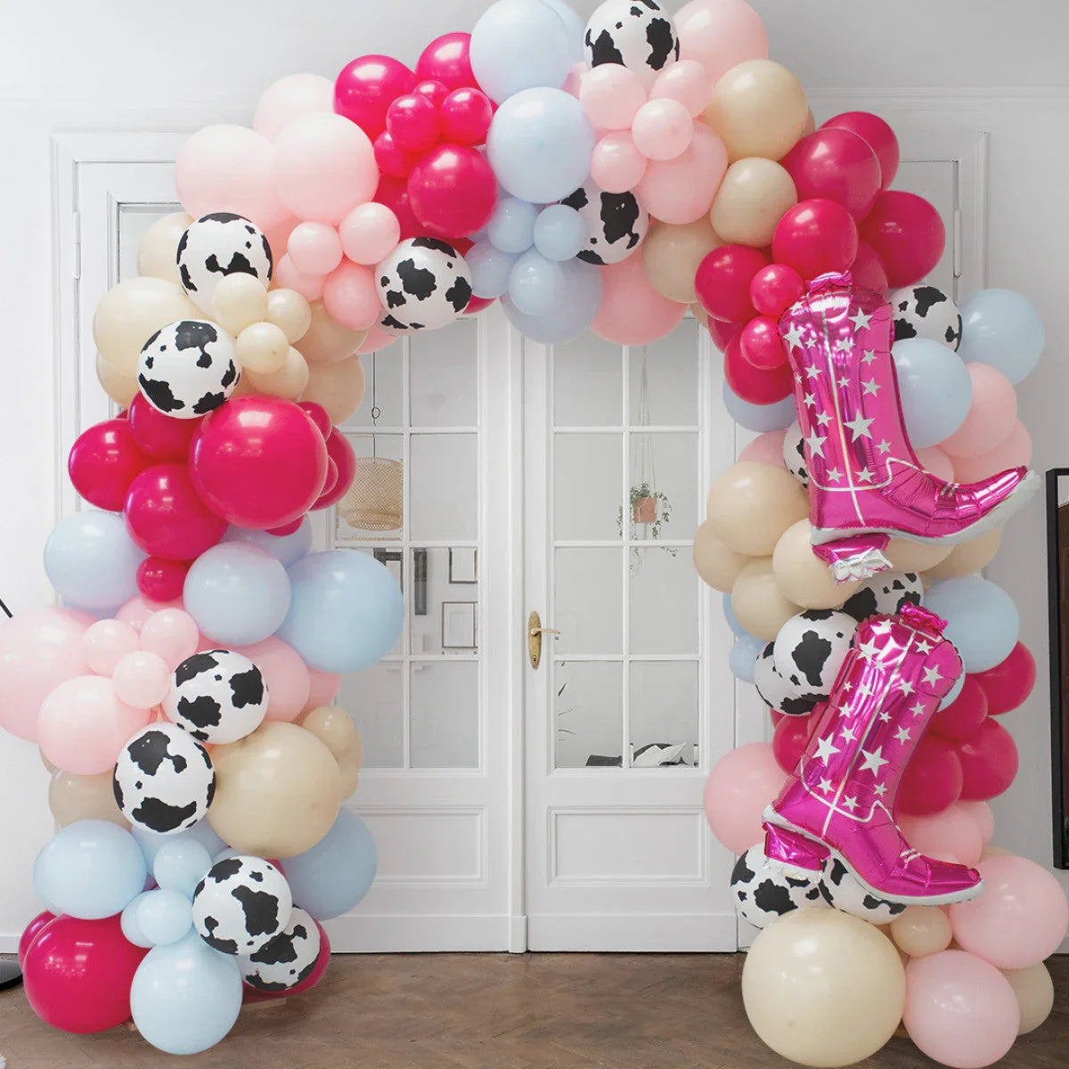 Colorful balloon arch with pink cowboy boot balloons and cow print balloons in front of white double doors