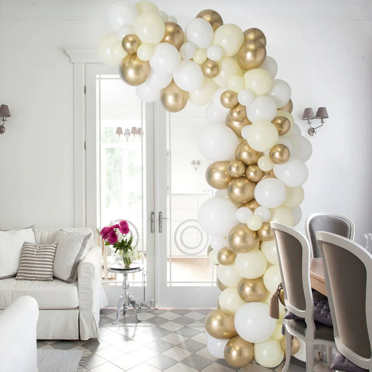 Asymmetric balloon arch in ivory, cream, and gold in a stylish white living and dining room