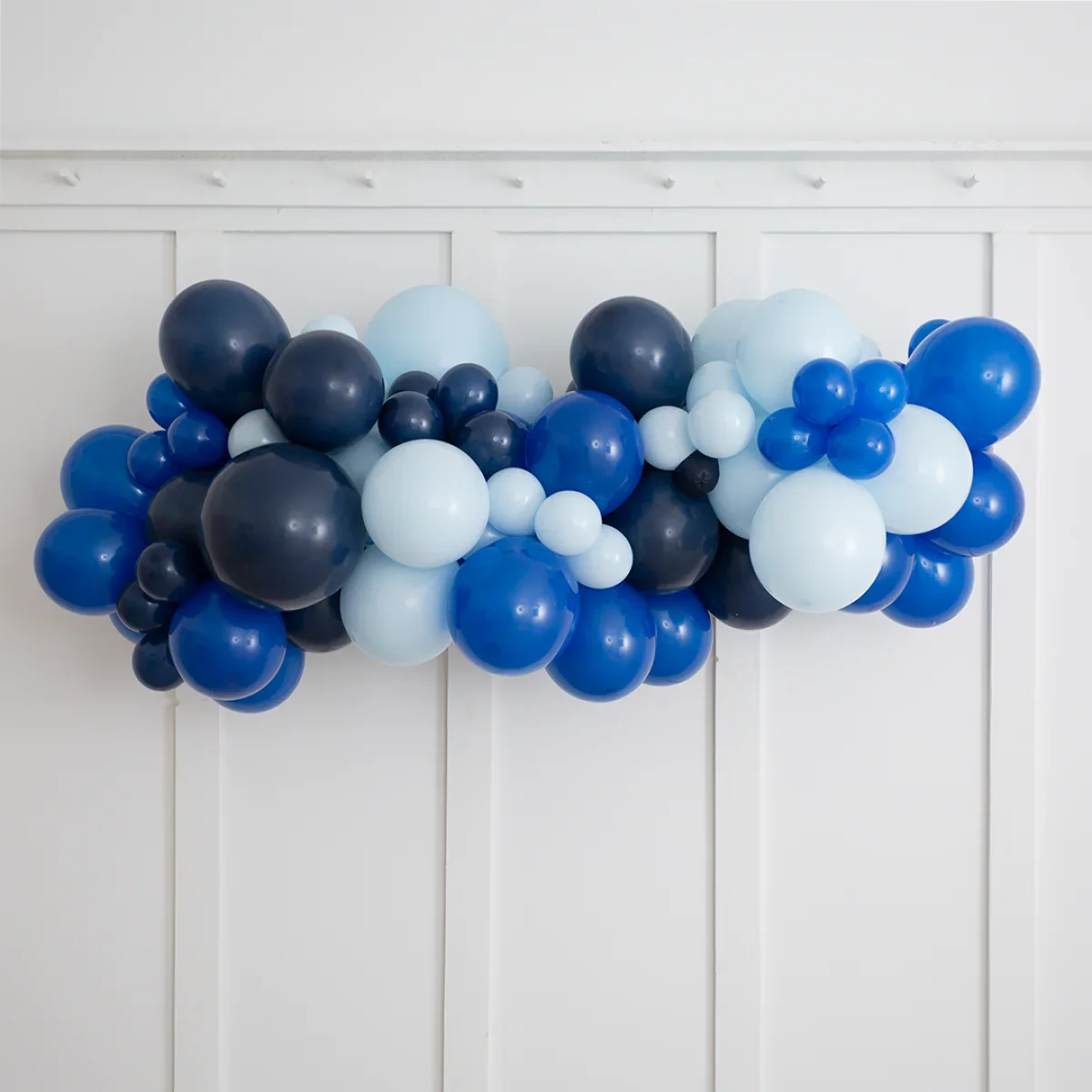Deep blue balloon garland with light and dark blue balloons on white paneled wall