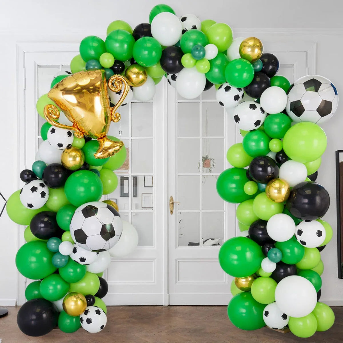 Green, black, white, and gold soccer-themed balloon arch with a gold trophy balloon inside