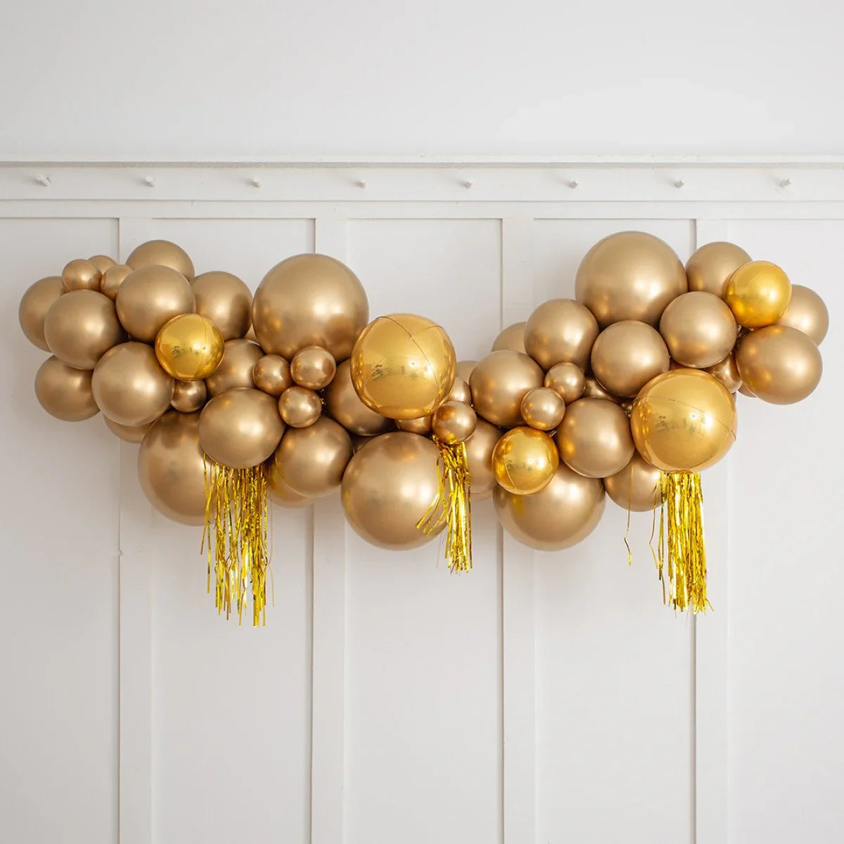 Gold party foil balloon garland with tassels on white paneled wall
