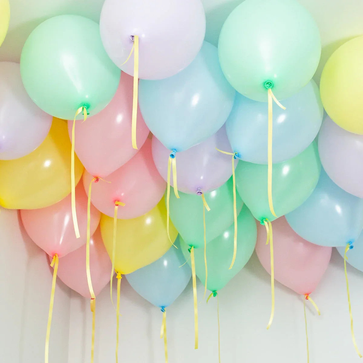 Cluster of pastel helium balloons with yellow ribbons floating on a white ceiling