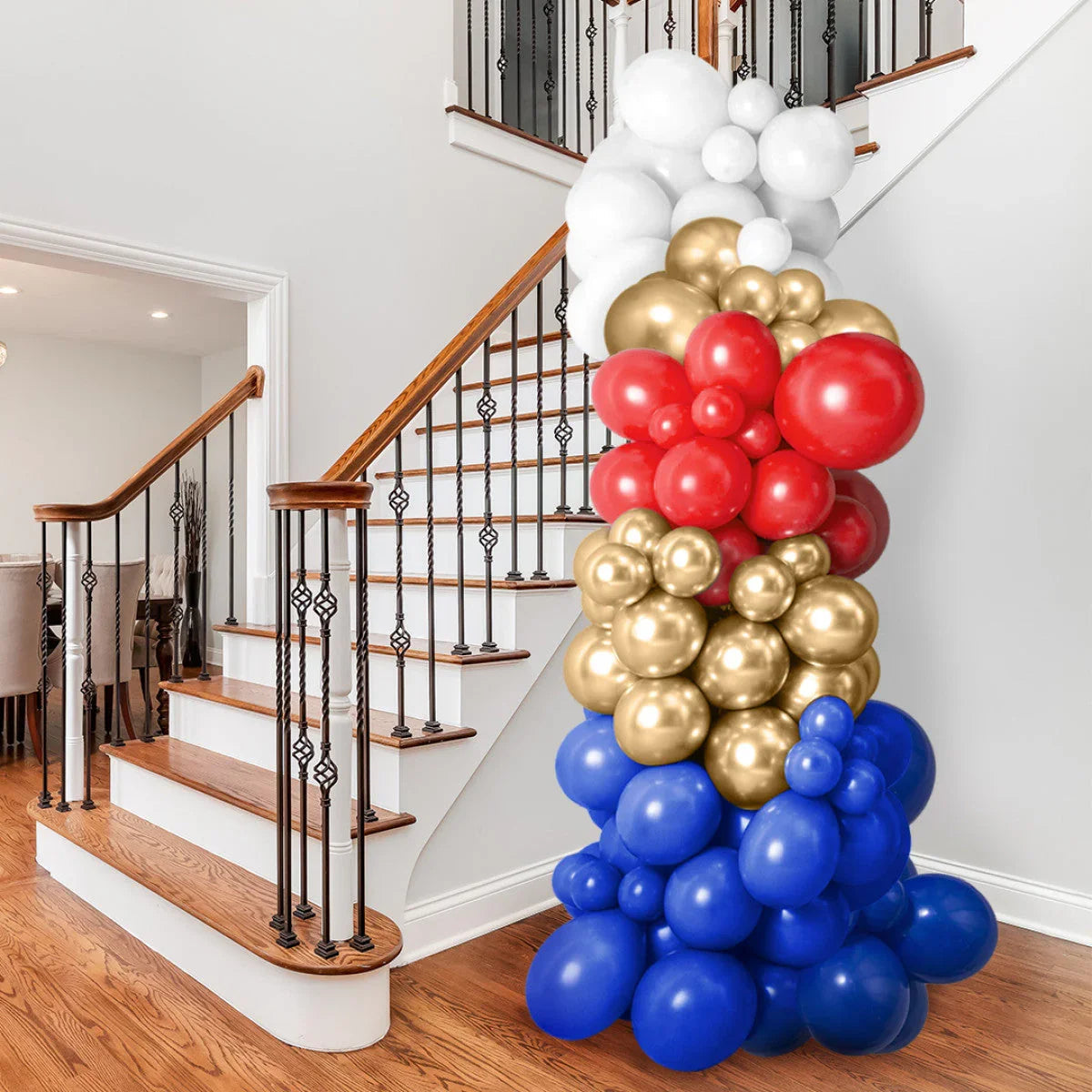 Colorful balloon pillar decoration in white, gold, red, and blue next to wooden staircase indoors