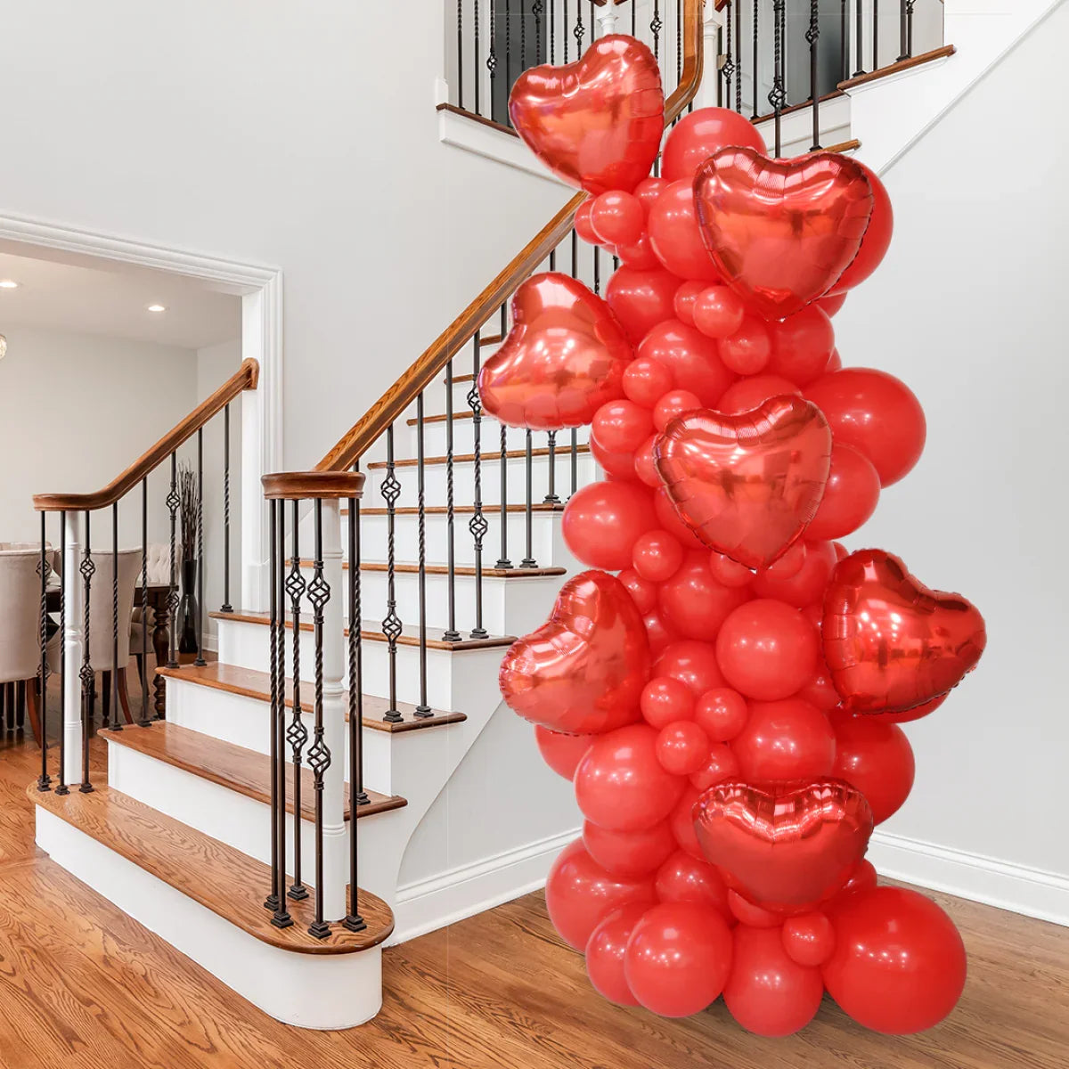 Red heart-shaped and round balloons stacked in a decorative pillar by a wooden staircase indoors