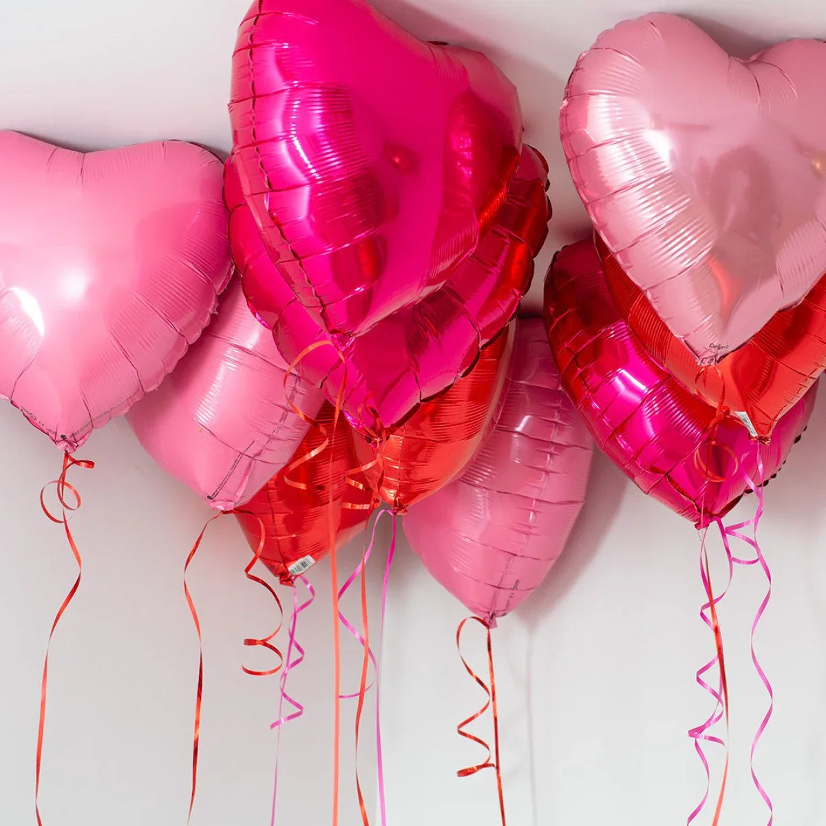 Cluster of red and pink heart-shaped helium balloons floating near ceiling with curly ribbons