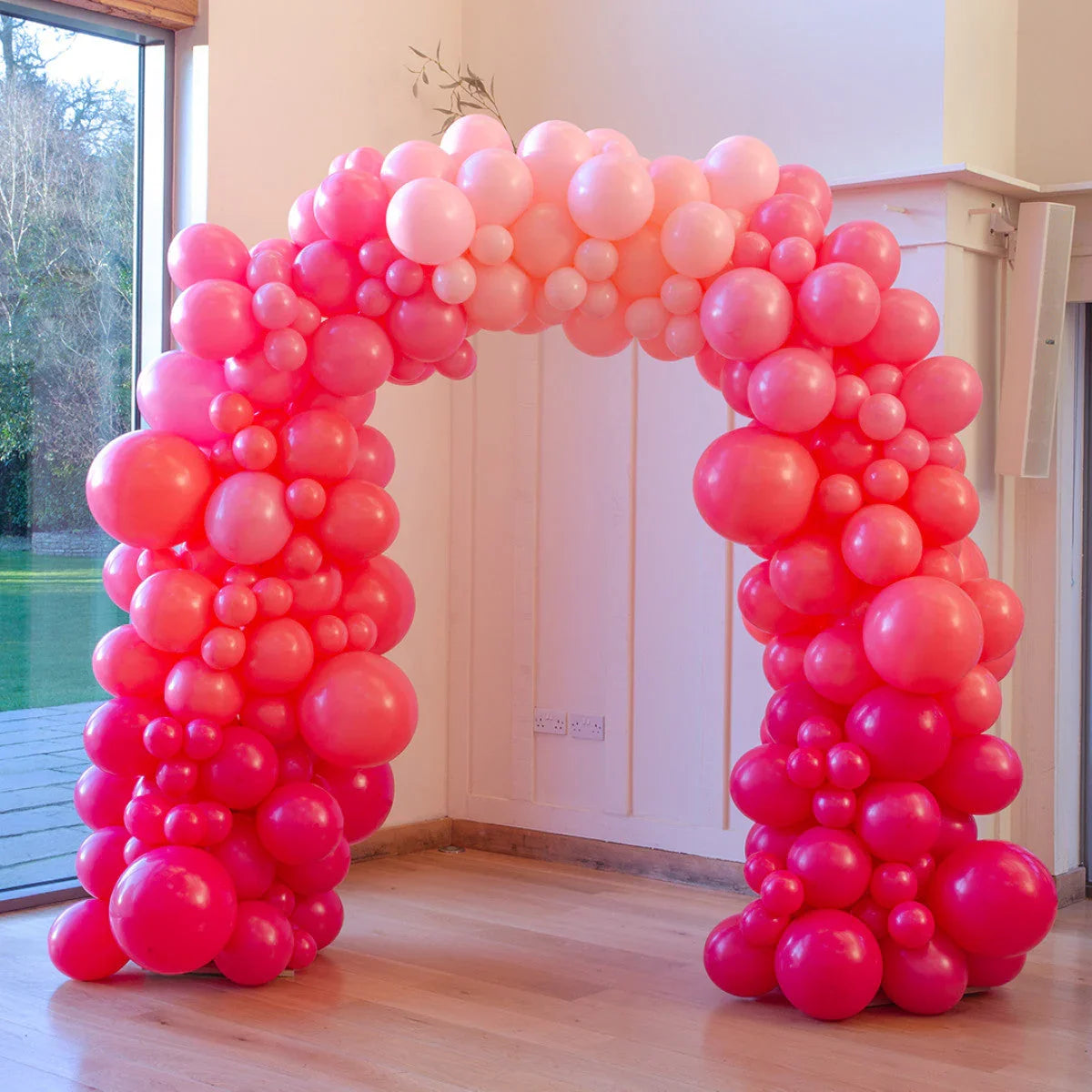 Pink ombré balloon arch with various sizes inside a bright room near large windows