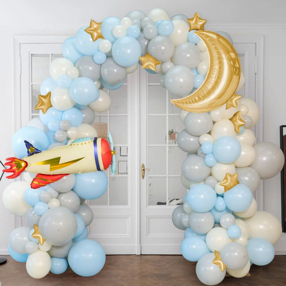 Blue, white, and gray balloon arch with gold stars, crescent moon, and rocket balloon decoration indoors