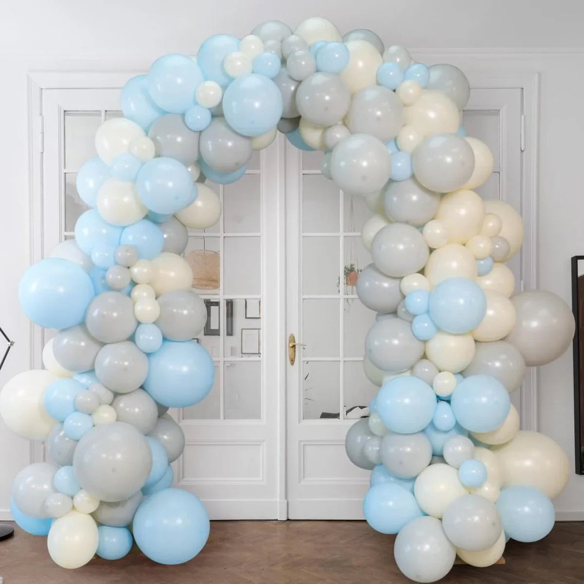 Decorative balloon arch in blue, gray, and cream colors set indoors in front of white double doors