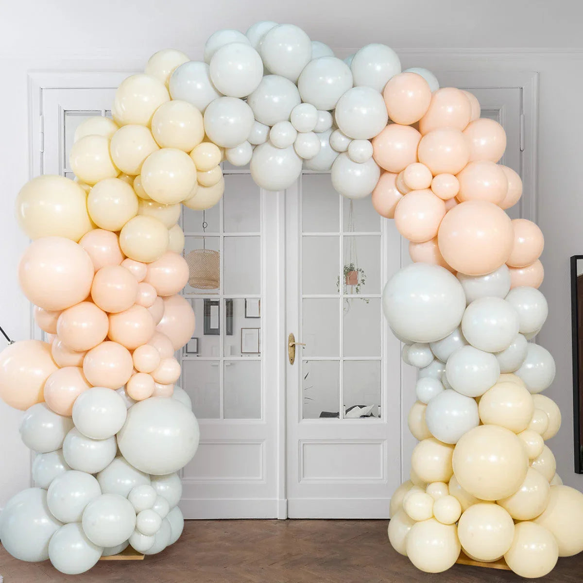 Nude, blush, and cream balloon arch decoration indoors in front of white doors
