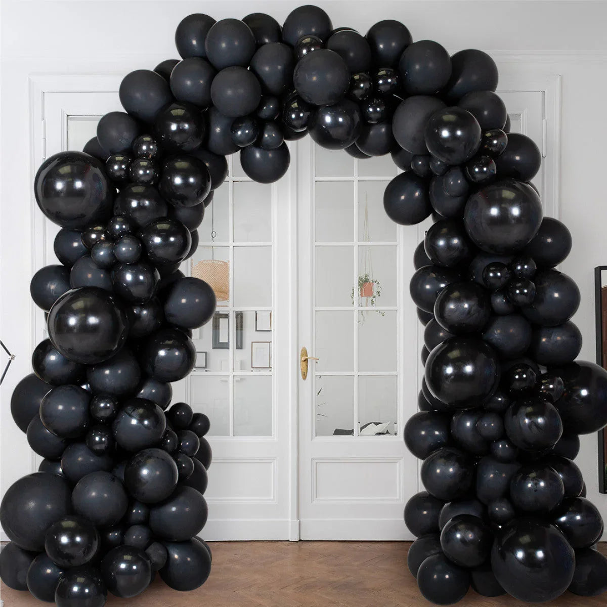 Large decorative balloon arch made of matte and glossy black balloons in front of white double doors