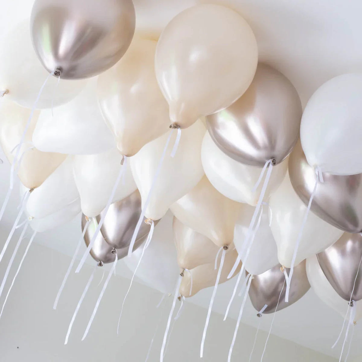 Helium balloons in pearl, white, and metallic silver floating on a white ceiling