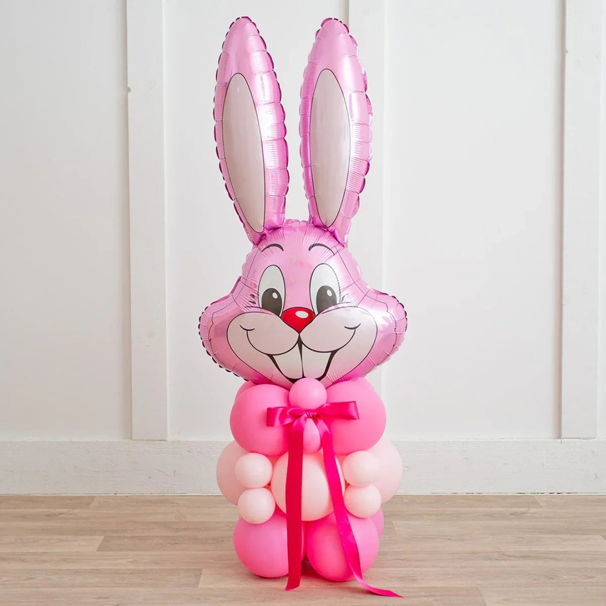 Pink Easter bunny balloon decoration with foil bunny face and tied pink ribbon on wooden floor