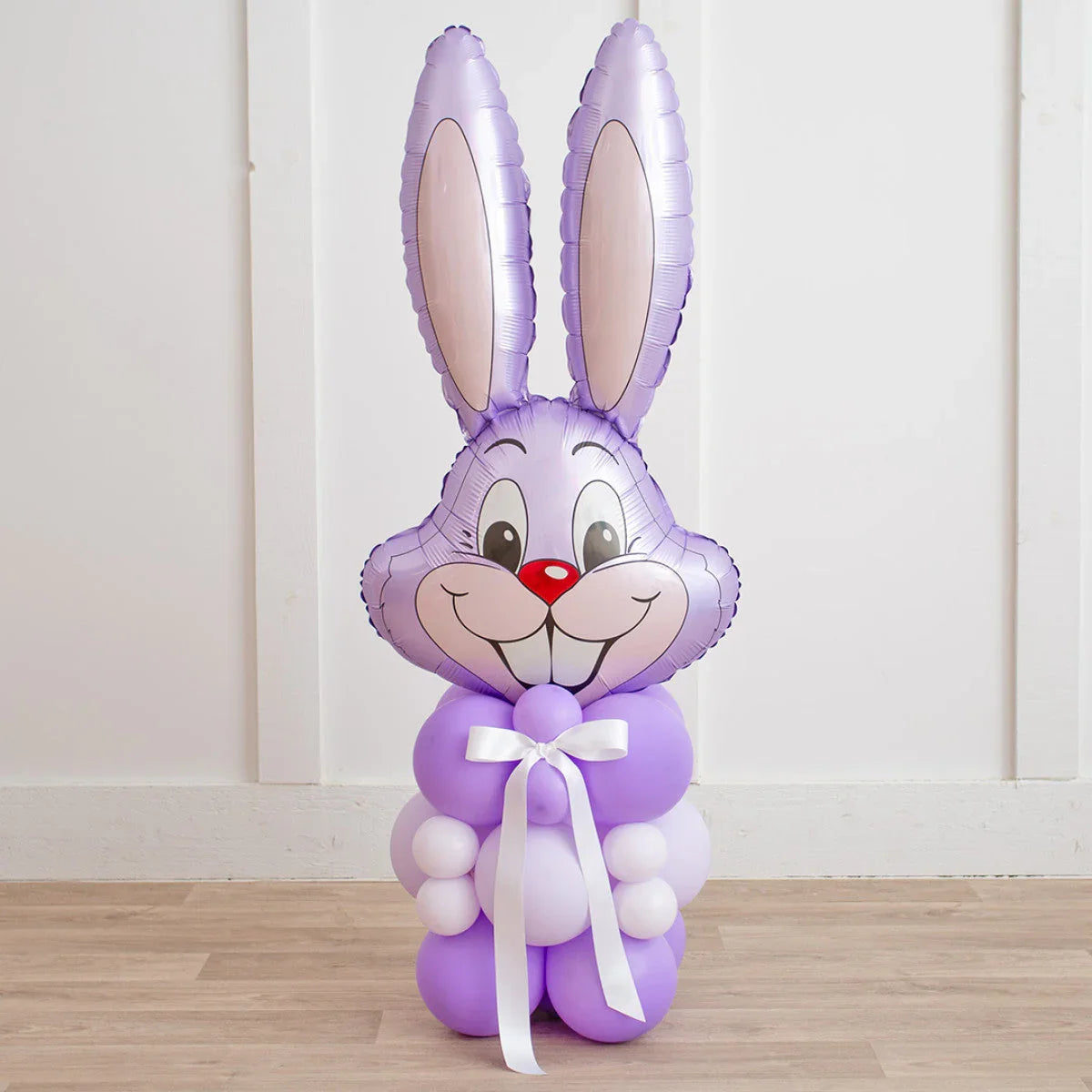 Purple Easter bunny balloon decoration with large ears and white ribbon on wooden floor