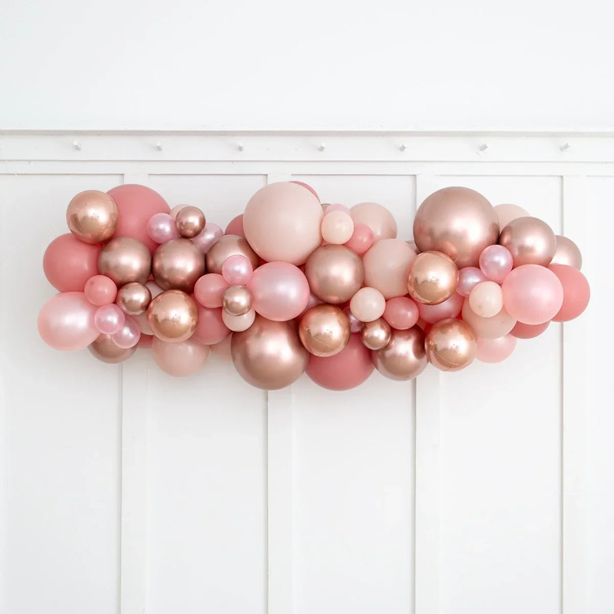 Rose gold and blush pink balloon garland decoration on white paneled wall