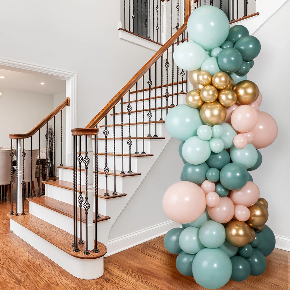 Sage green, gold, and blush pink balloon pillar decorating hardwood stairs with wrought iron railing