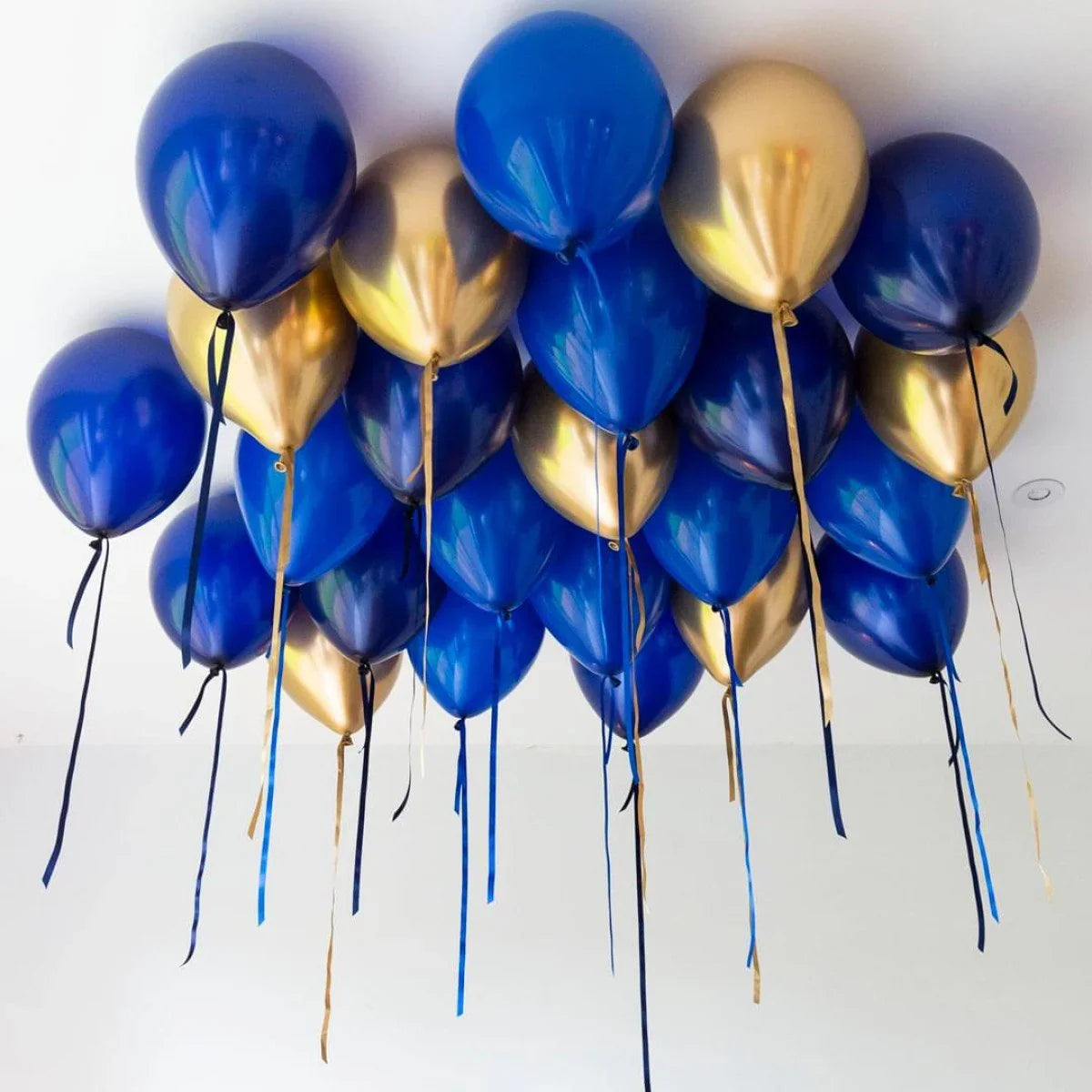 Cluster of blue and gold helium balloons floating near a white ceiling with attached ribbons