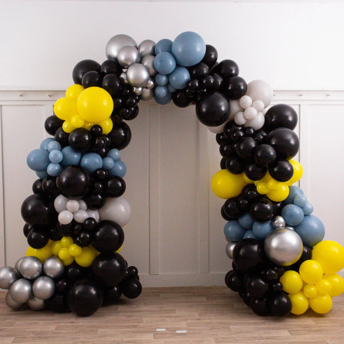 Bespoke balloon arch with black, yellow, silver, blue, and white balloons indoors on wooden floor