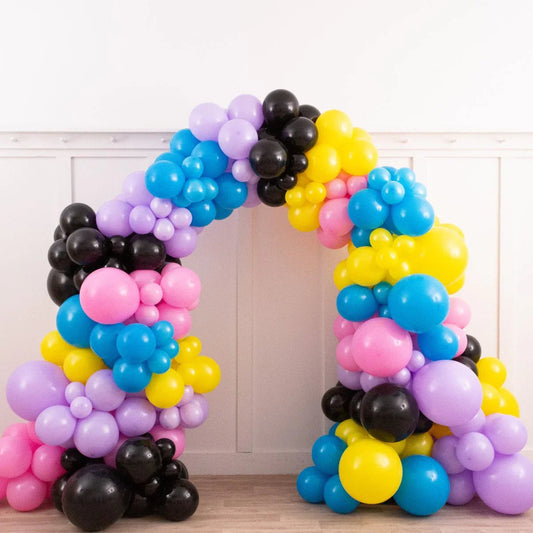 Colorful balloon arch with blue, yellow, pink, purple, and black balloons in an indoor setting