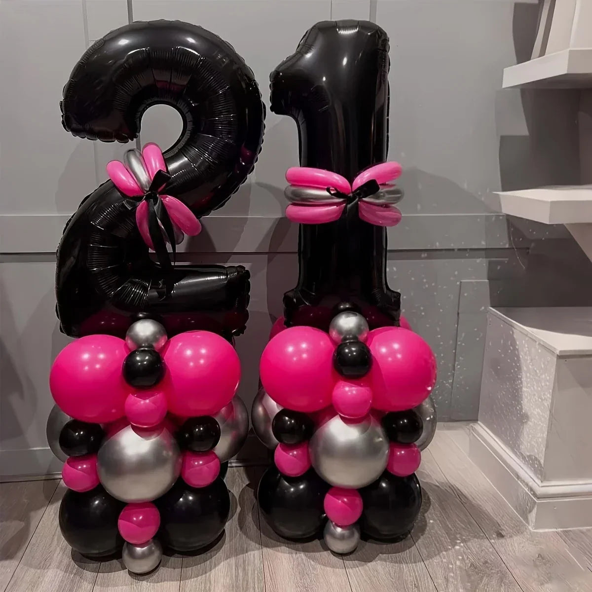 Black number 21 balloons decorated with pink and silver balloon clusters on floor indoors