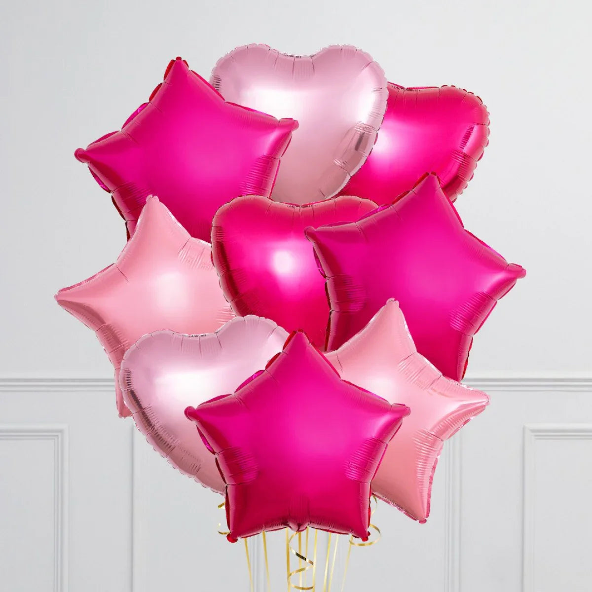 Bright pink and baby pink heart and star shaped foil balloons bunch against white wall