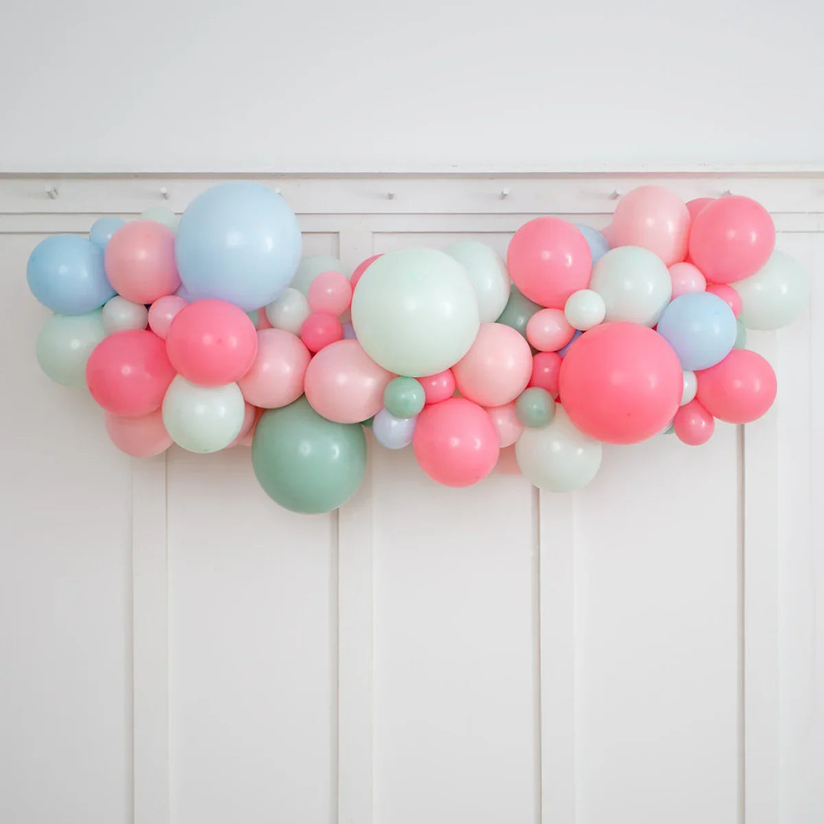 Colorful pastel balloon garland with pink, blue, green, and white balloons on white wall