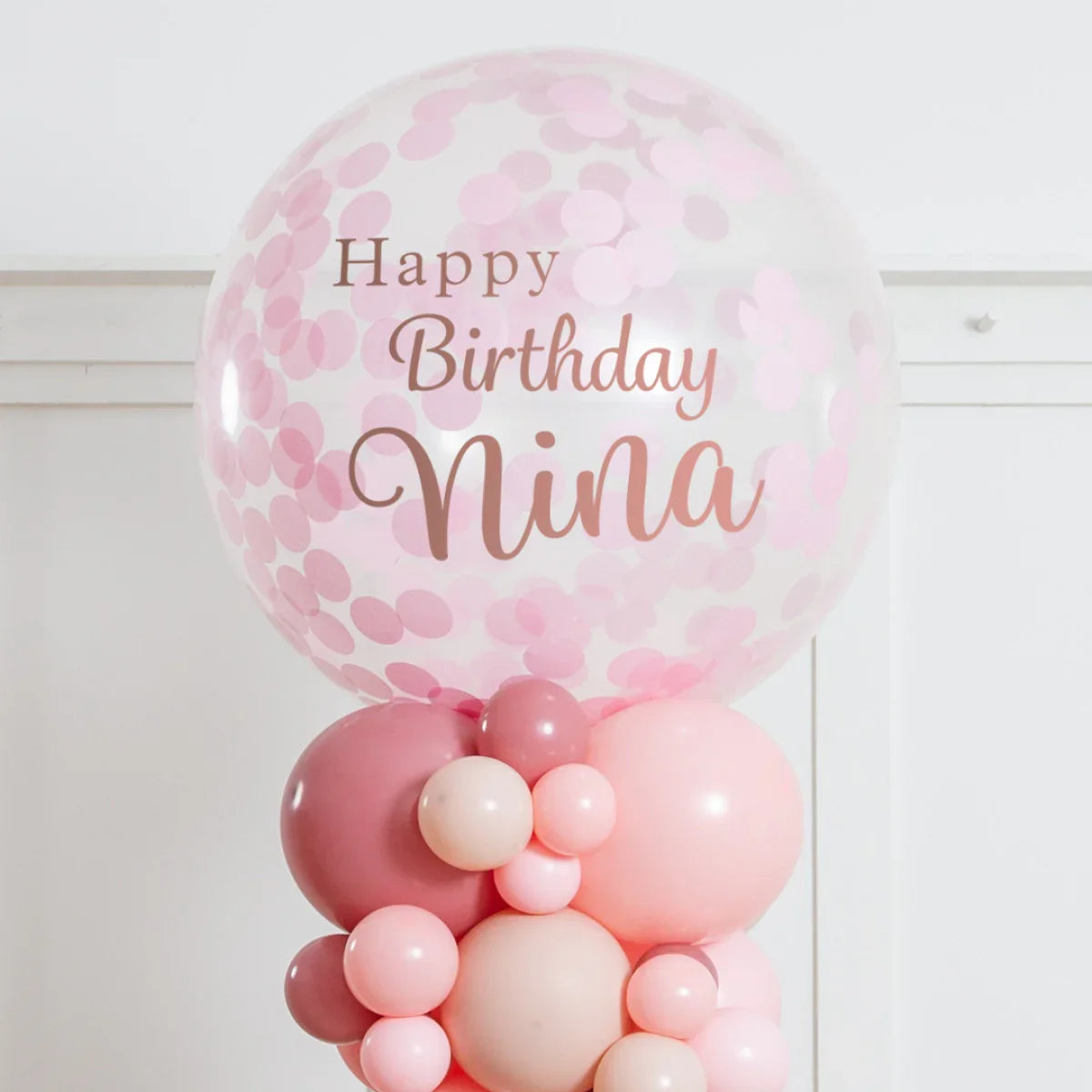 Pink confetti balloon bouquet with Happy Birthday Nina text, pastel party decoration