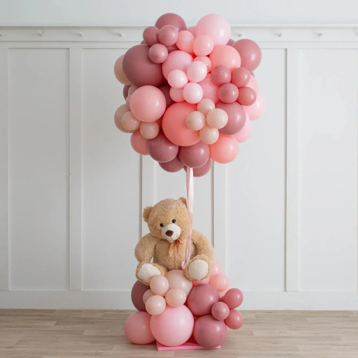 Teddy bear sitting in pink and mauve balloon hot air balloon arrangement indoors