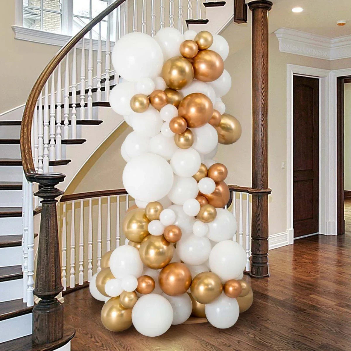 Elegant balloon pillar with white, gold, and copper balloons displayed at a curved staircase in a modern home
