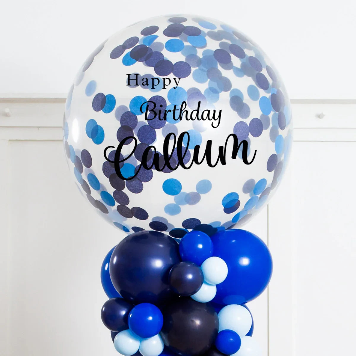 Large clear balloon with blue confetti and text Happy Birthday Callum on a pillar of blue balloons