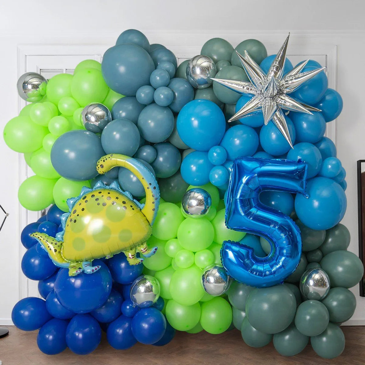 Colorful balloon wall with green, blue, and gray balloons, silver spheres, dinosaur balloon, and blue number 5 balloon
