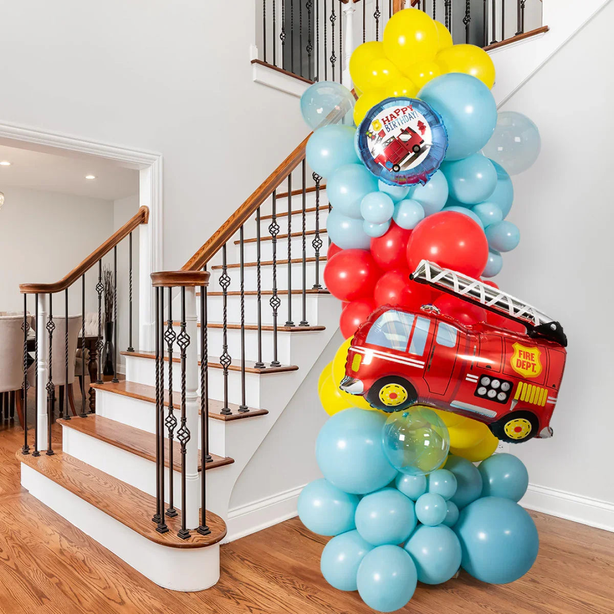 Colorful fire engine themed balloon pillar with red, yellow, and blue balloons by staircase indoors
