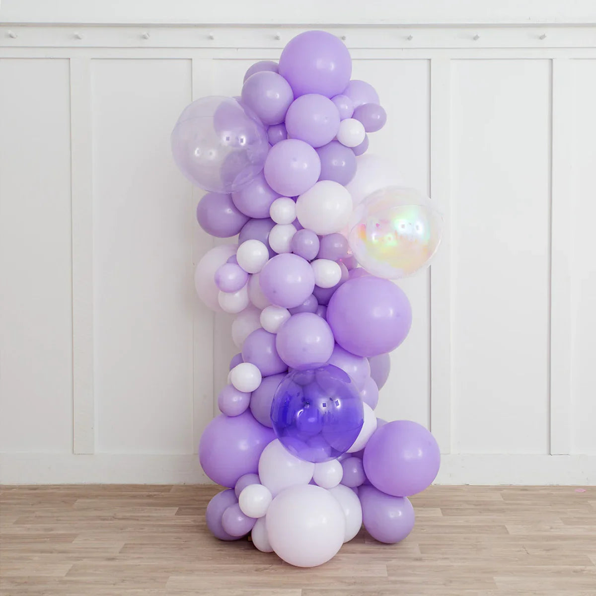 Lavender and white inflated balloon pillar with clear and purple balloons against white wall