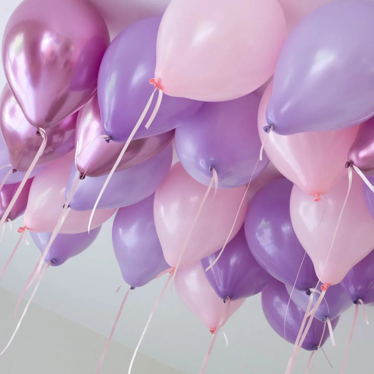 Lavender, rose gold, and pink helium balloons floating on ceiling with ribbons
