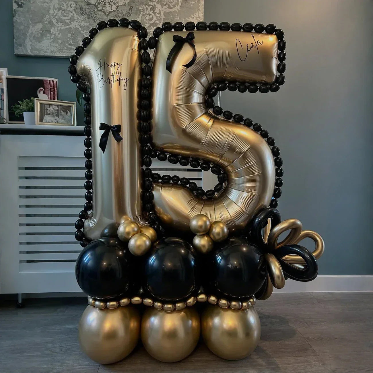 Golden number 15 birthday balloon decorated with black bows, black and gold balloons base indoors