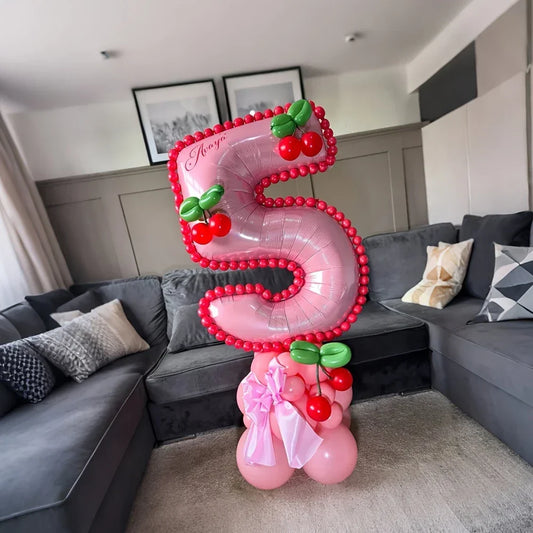 Pink number 5 balloon decorated with red and green cherry balloons and pink bows in a modern living room