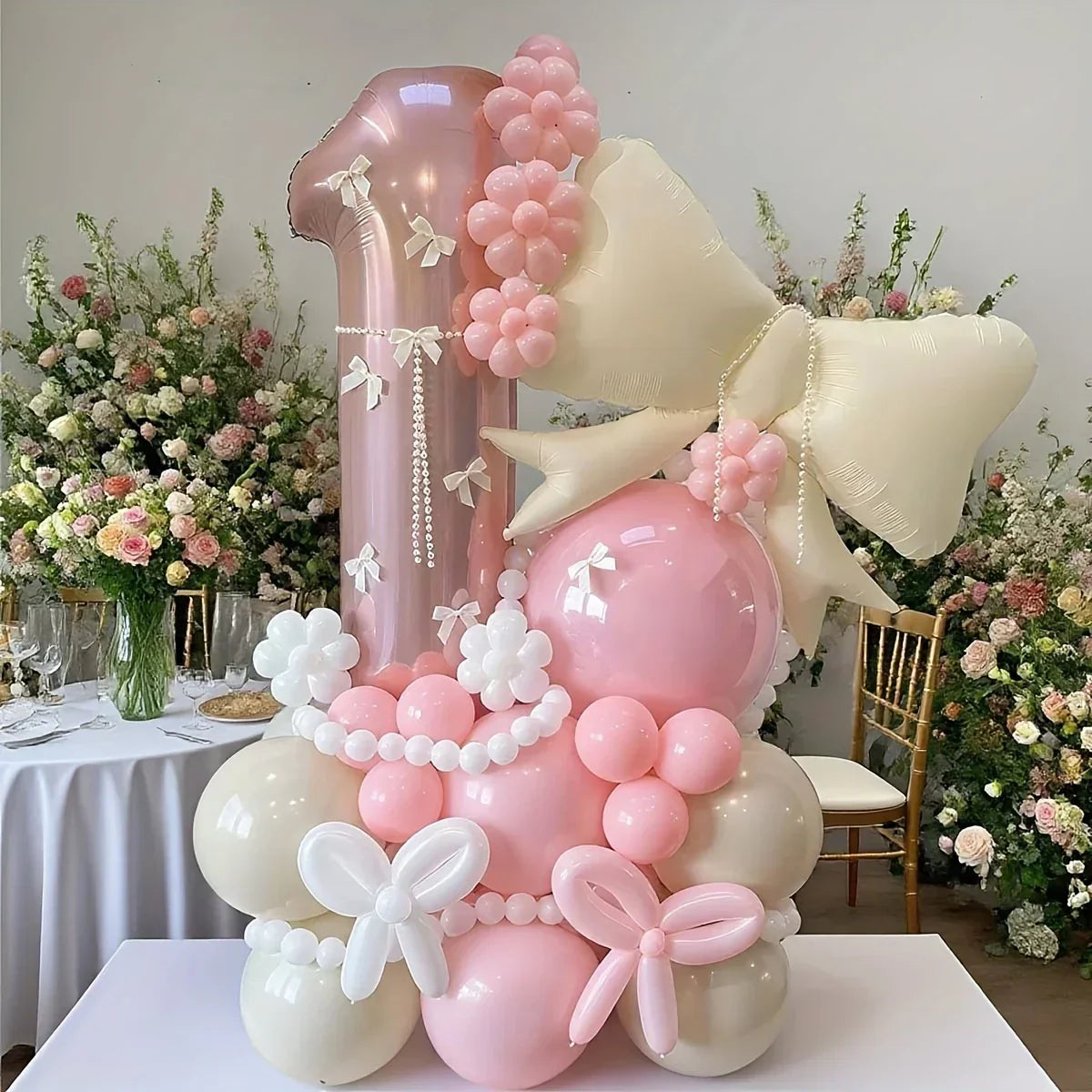 Pink and cream first birthday balloon arrangement with flowers and butterflies at event venue
