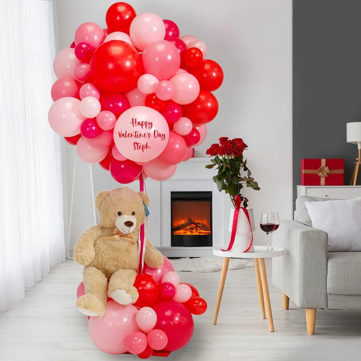 Valentine's Day balloon installation with teddy bear and red roses in cozy living room