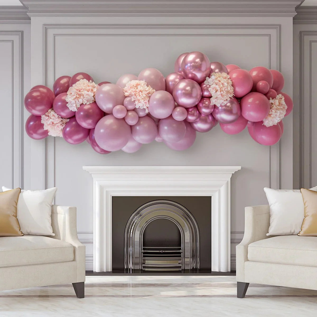 Pink and mauve balloon garland with floral accents above white fireplace in elegant living room