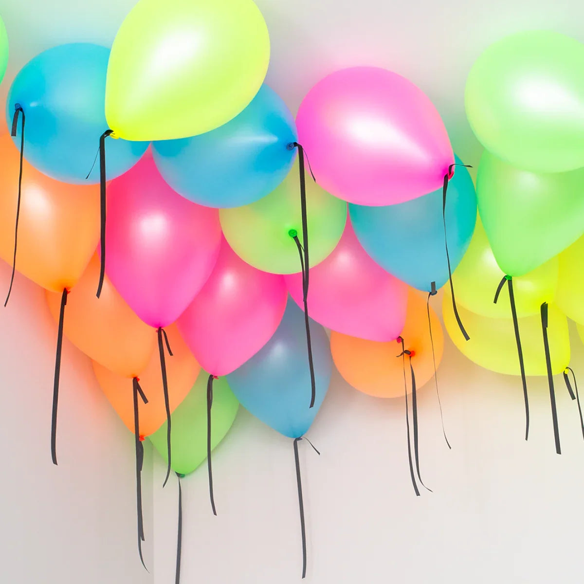 Colorful neon balloons clustered close to a ceiling with black ribbons hanging down