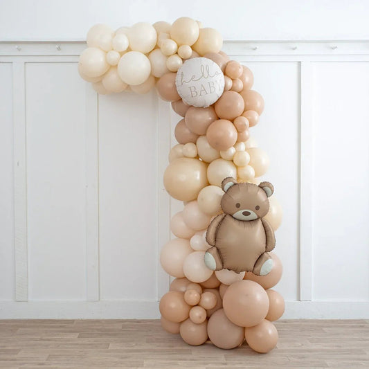 Neutral beige asymmetric balloon arch with a teddy bear and hello baby round balloon indoors