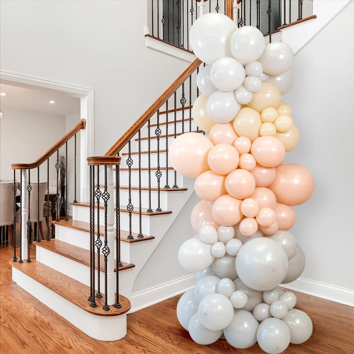 Nude, blush, and white balloon pillar decoration next to wooden staircase in a modern home
