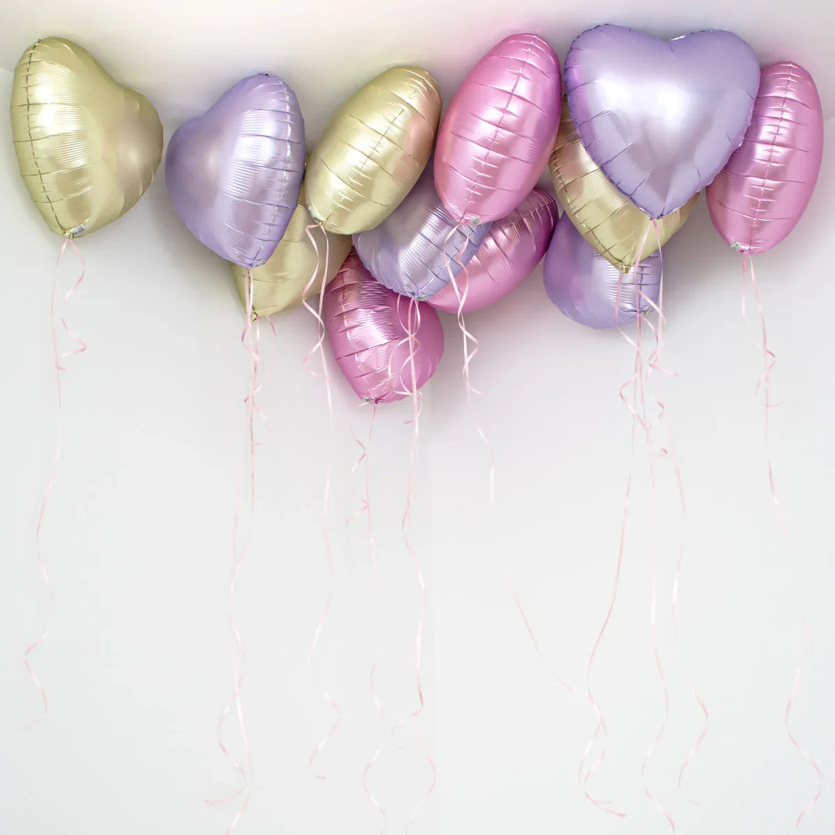 Pastel pink, purple, and gold heart-shaped foil helium balloons floating near ceiling