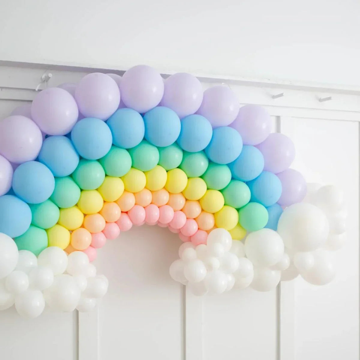 Pastel rainbow balloon arch with white balloon clouds on white paneled wall
