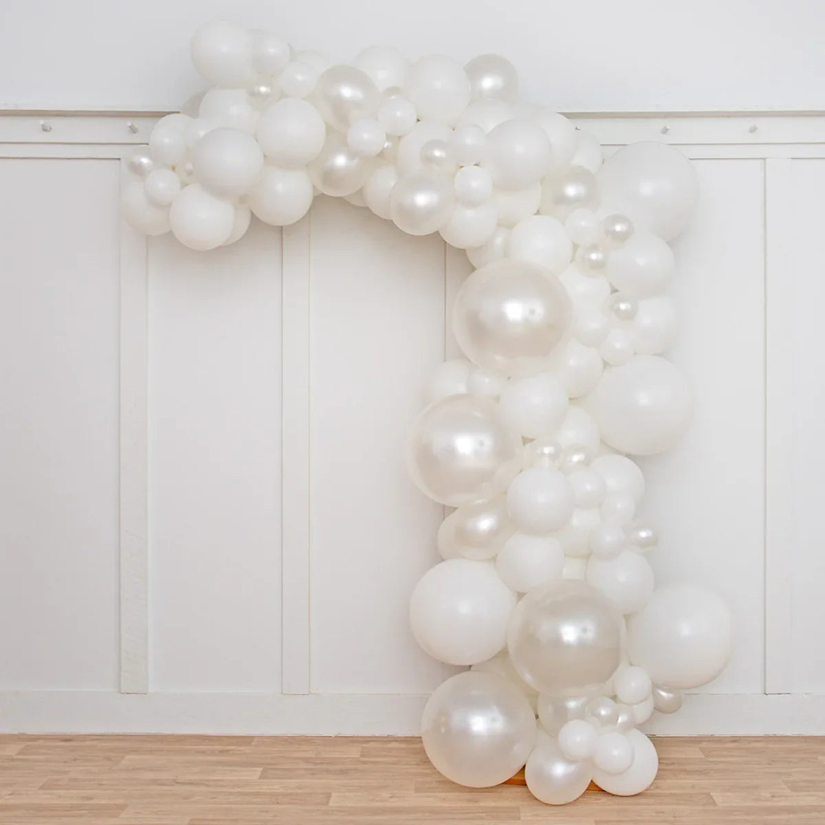 Asymmetric white and pearl balloon arch decoration against white paneled wall and wooden floor